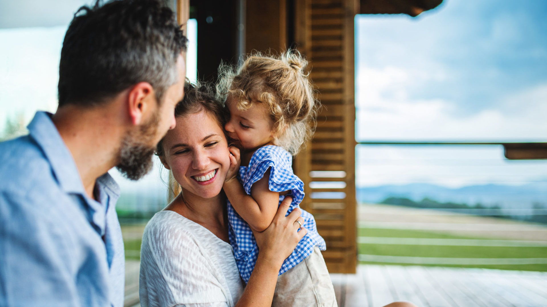 Family,With,Small,Daughter,Sitting,On,Patio,Of,Wooden,Cabin,